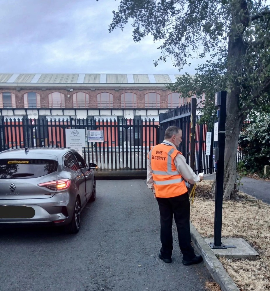 DMS security officer in an orange hi-vis vest checking a vehicle at a car park gate