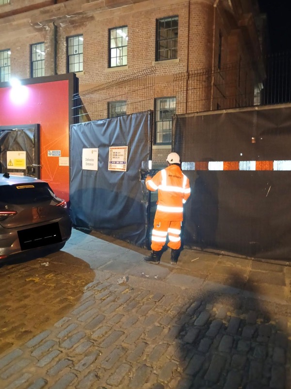 DMS security officer in hi-vis at a site gate at night