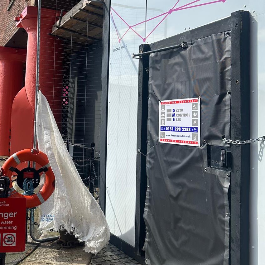 Site hoarding door secured with a chain and lock, with DMS warning signage
