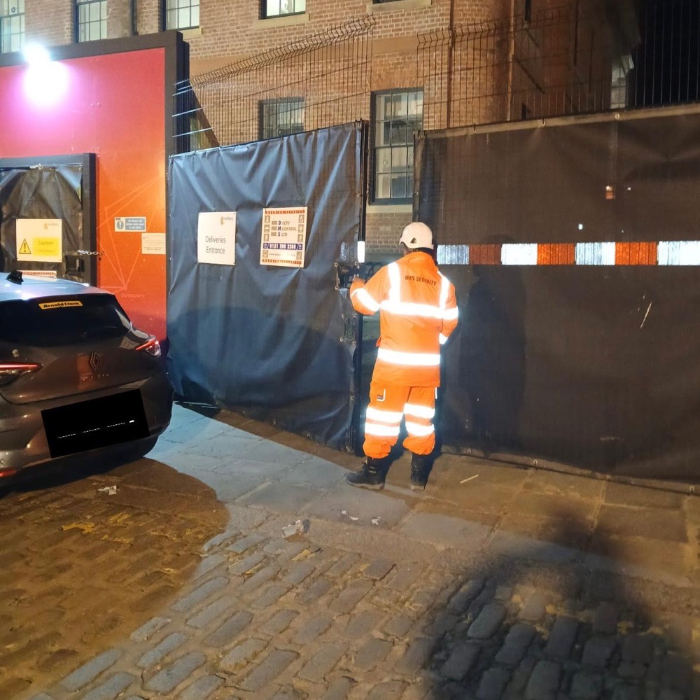 DMS security officer in hi-vis at a site gate at night
